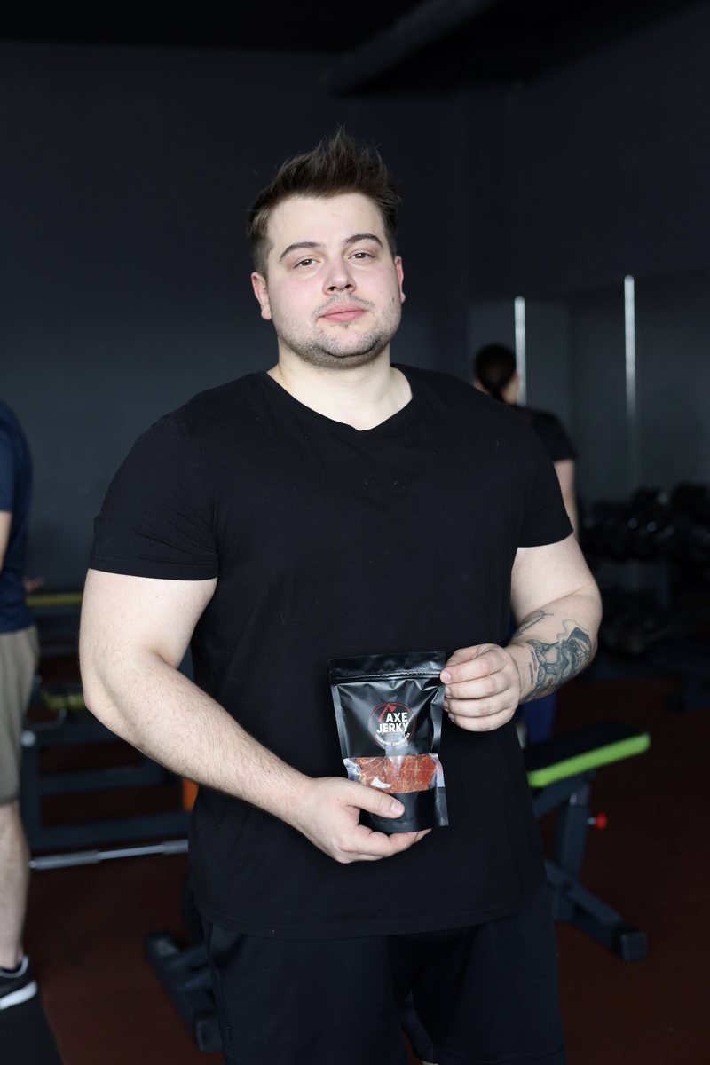Чоловік у спортзалі тримає пачку курячих джерків AXE Jerky