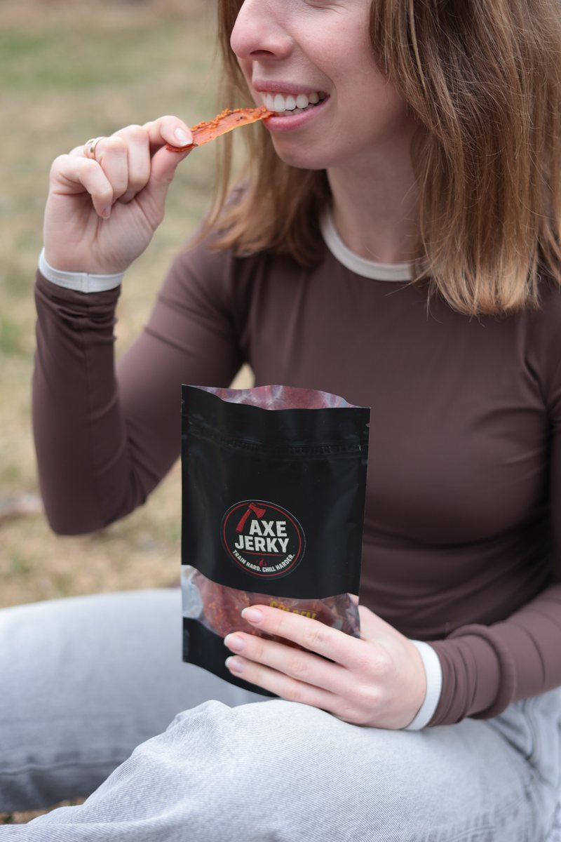 Дівчина на природі їсть курячі джерки AXE Jerky